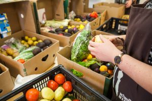 Boxes of fresh produce on table, with hands of a person being shown sorting items.