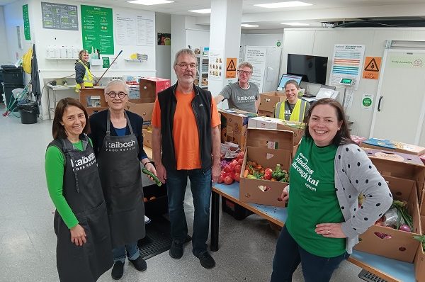 Six people stand near tables with boxes of fresh produce.